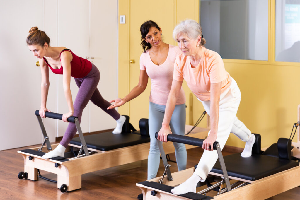 Instrutora de pilates e duas mulheres fazendo pilates no aparelho